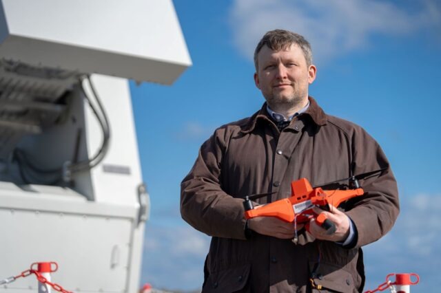 A member of DE&S' Directed Energy Weapons team holds a drone in front of an RF DEW demonstrator