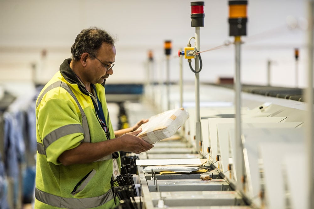 Integrated logistics member of staff in hi vis jacket looking at parcel